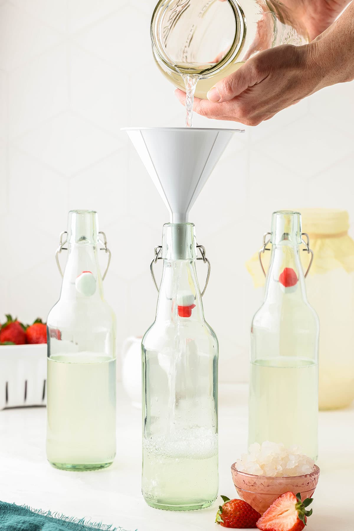 Flip top bottles with water kefir, a funnel in the front one with water kefir pouring into it. 