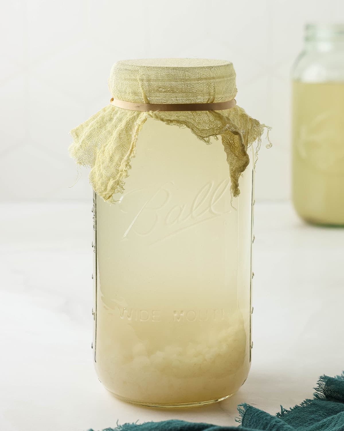 Jar of water kefir with a cheesecloth secured to the top, ready to ferment.