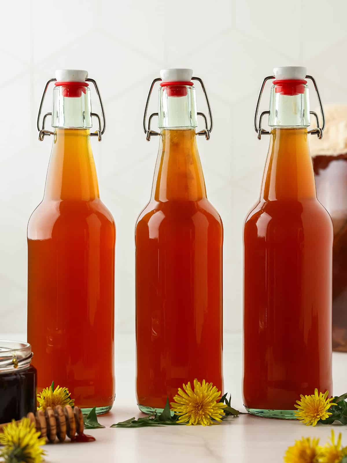 3 bottles of dandelion kombucha closed and ready for second fermentation, with fresh dandelions surrounding. 
