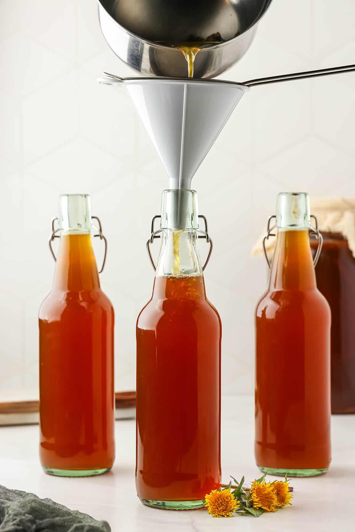 Cooled dandelion tea pouring through a funnel into the bottles with kombucha in them. 