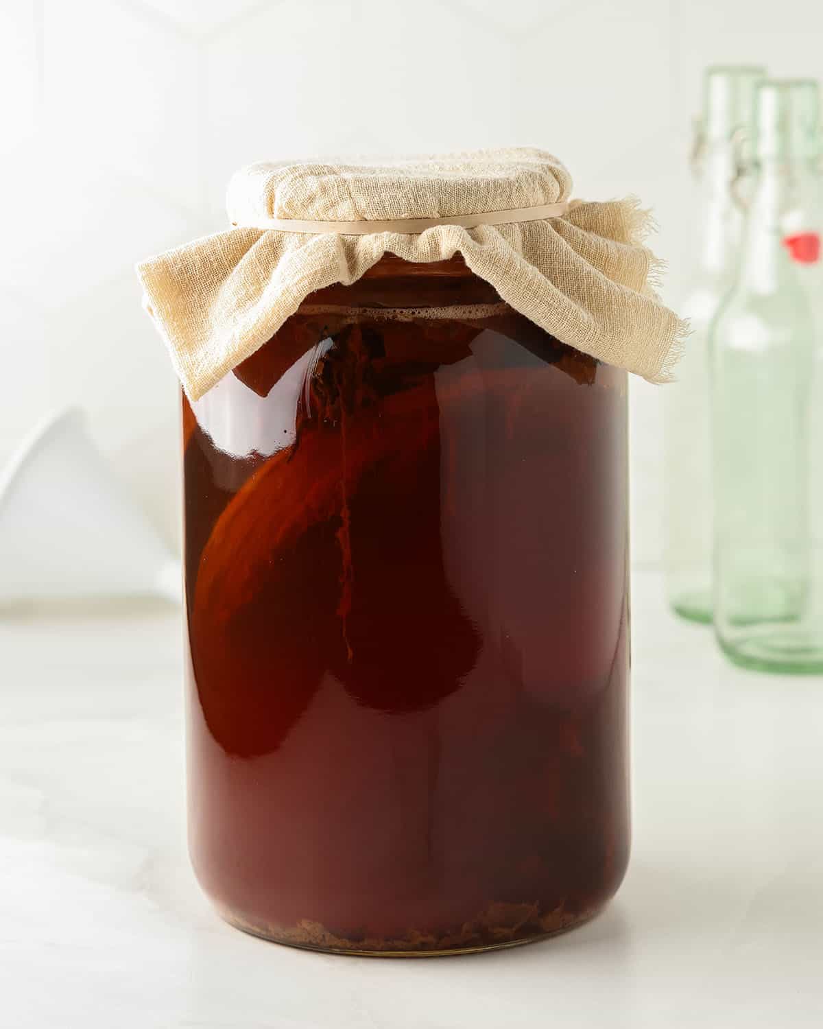 A gallon jar brewing kombucha with a cheesecloth secured to the top. 