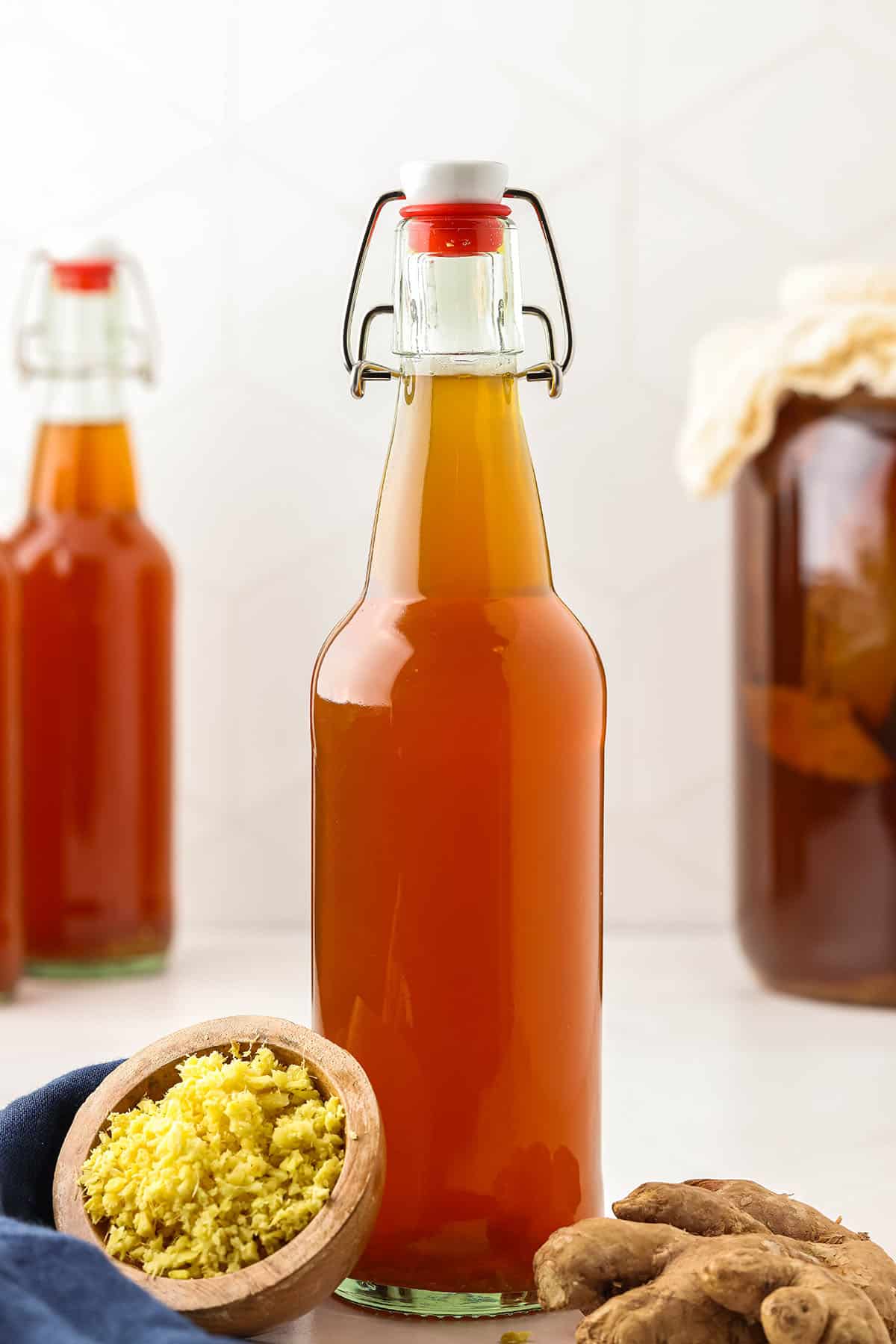 Bottles of ginger kombucha that are starting to bubble, with minced ginger and a fresh ginger root sitting next to it. 