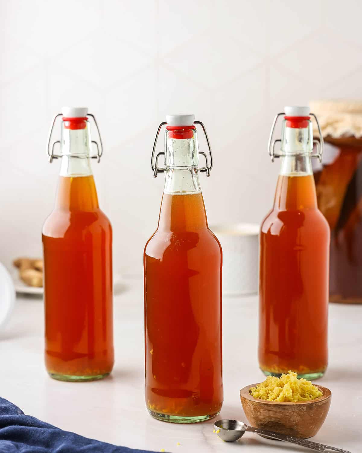 Ginger kombucha in bottles with caps on, ready to ferment. With a small bowl of minced ginger. 