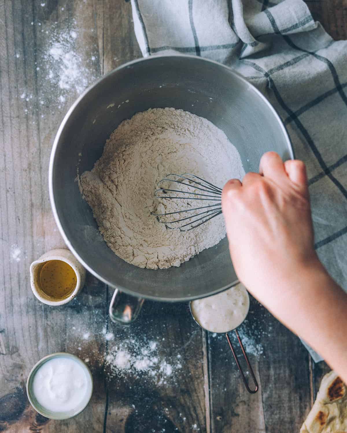 A whisk mixing the dry ingredients to make naan bread, top view. 