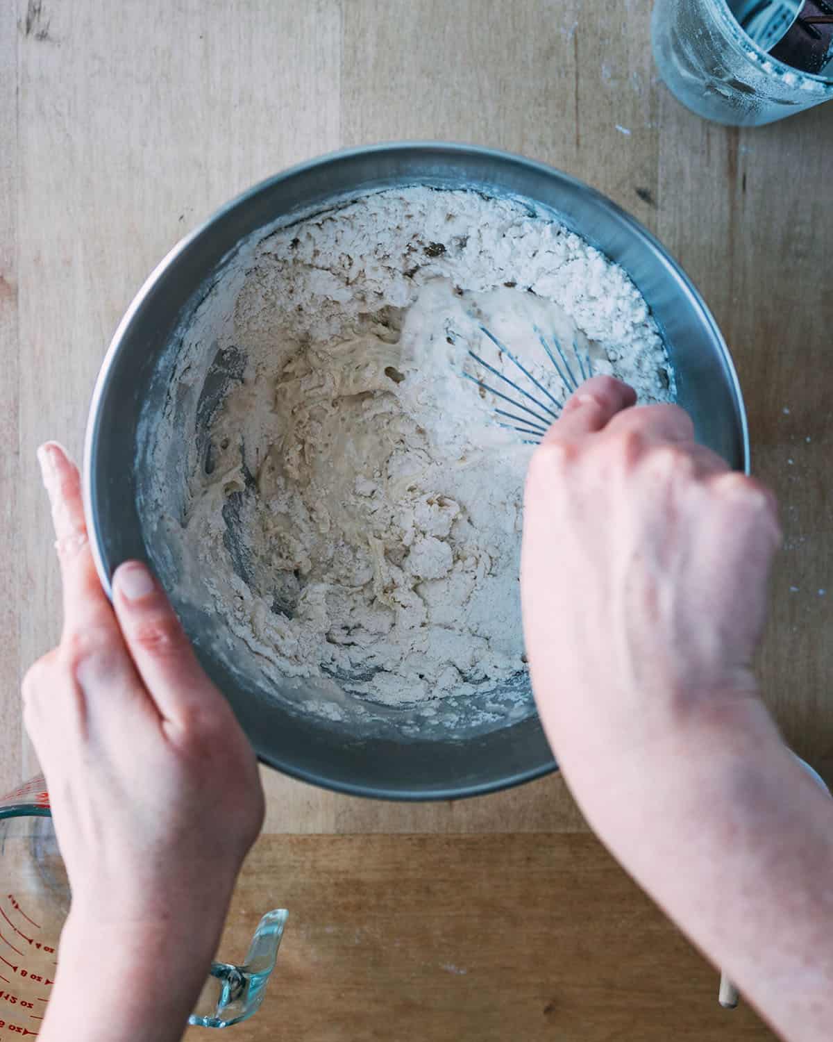 Hands stirring together the sourdough pizza dough ingredients. 