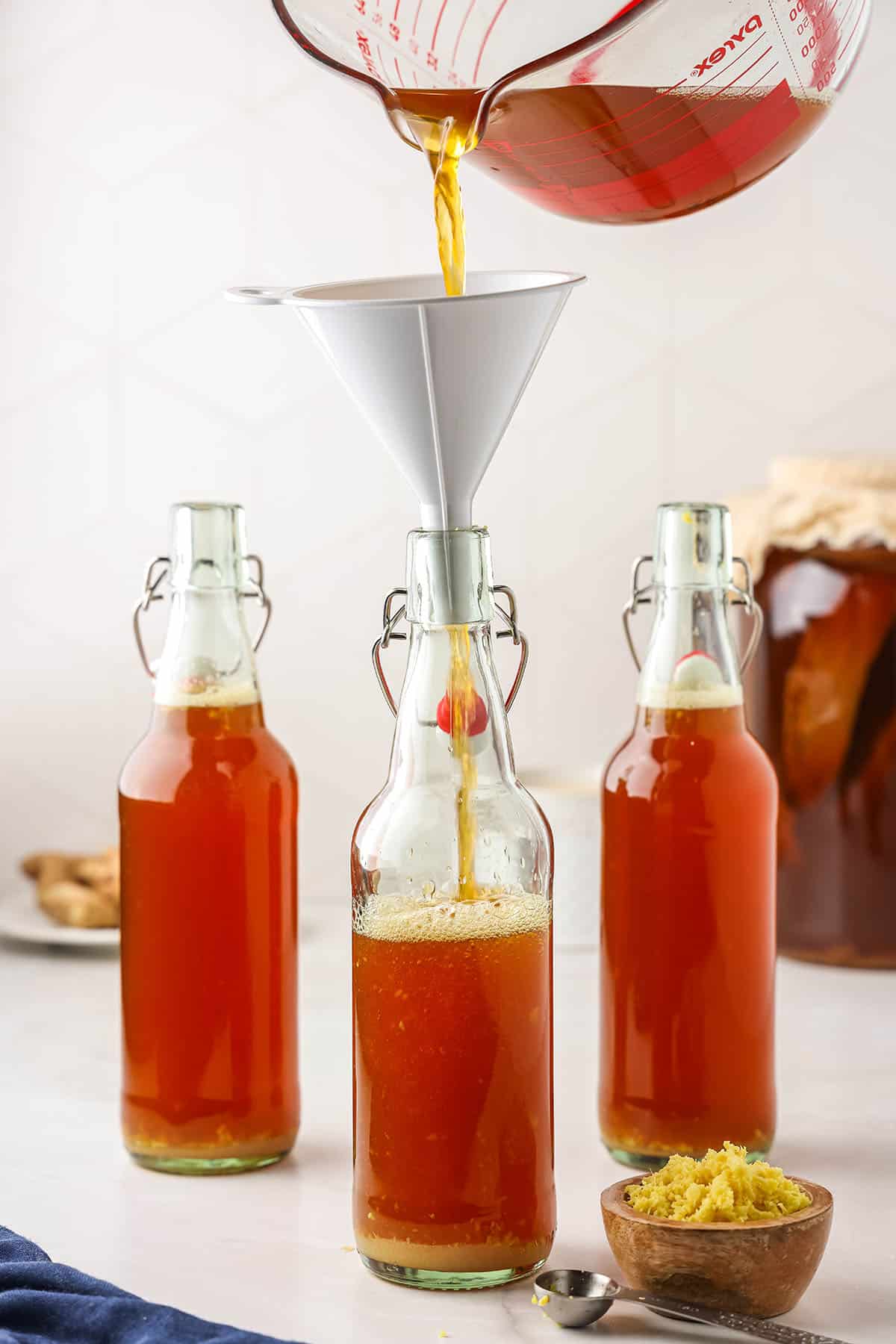 Kombucha pouring from into flip top bottles with a funnel for a second ferment. 