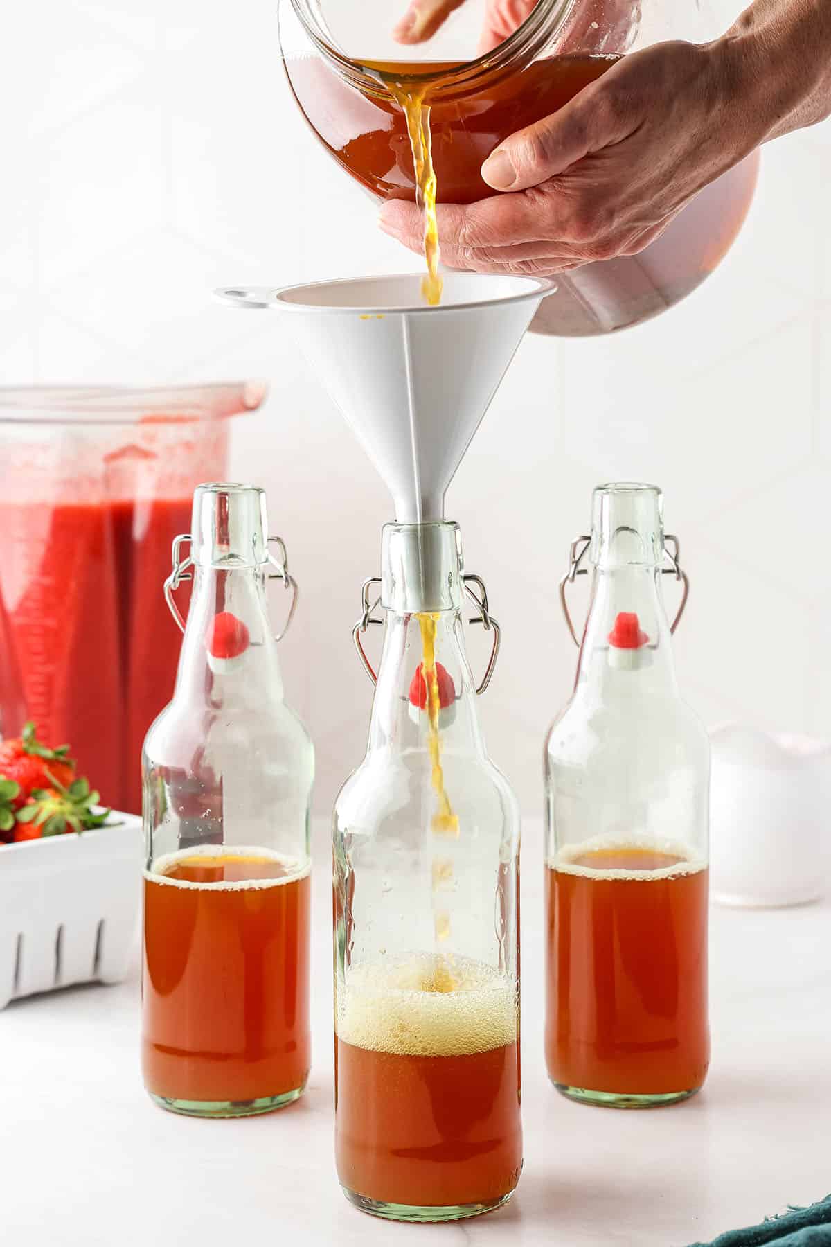 Kombucha being poured into flip top bottles with a funnel. 