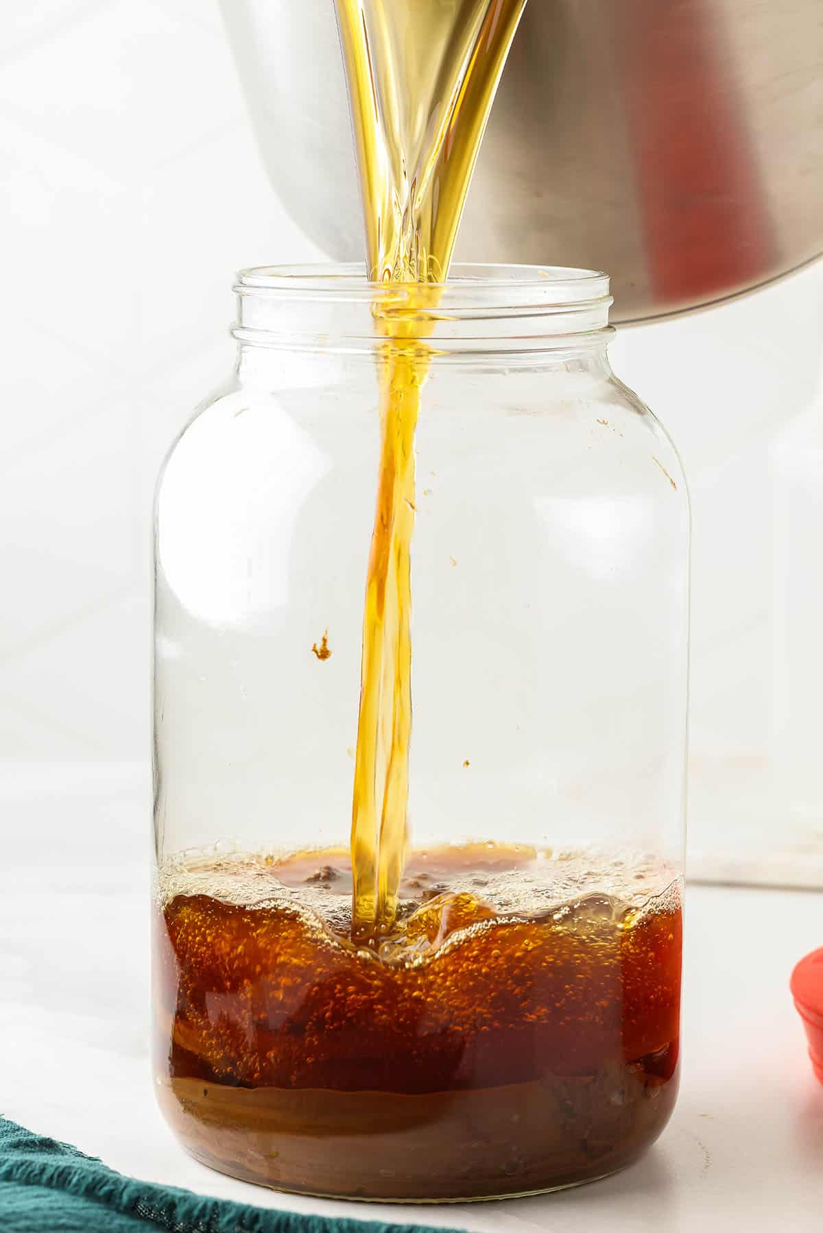 Tea pouring from the pot into a large glass jar. 