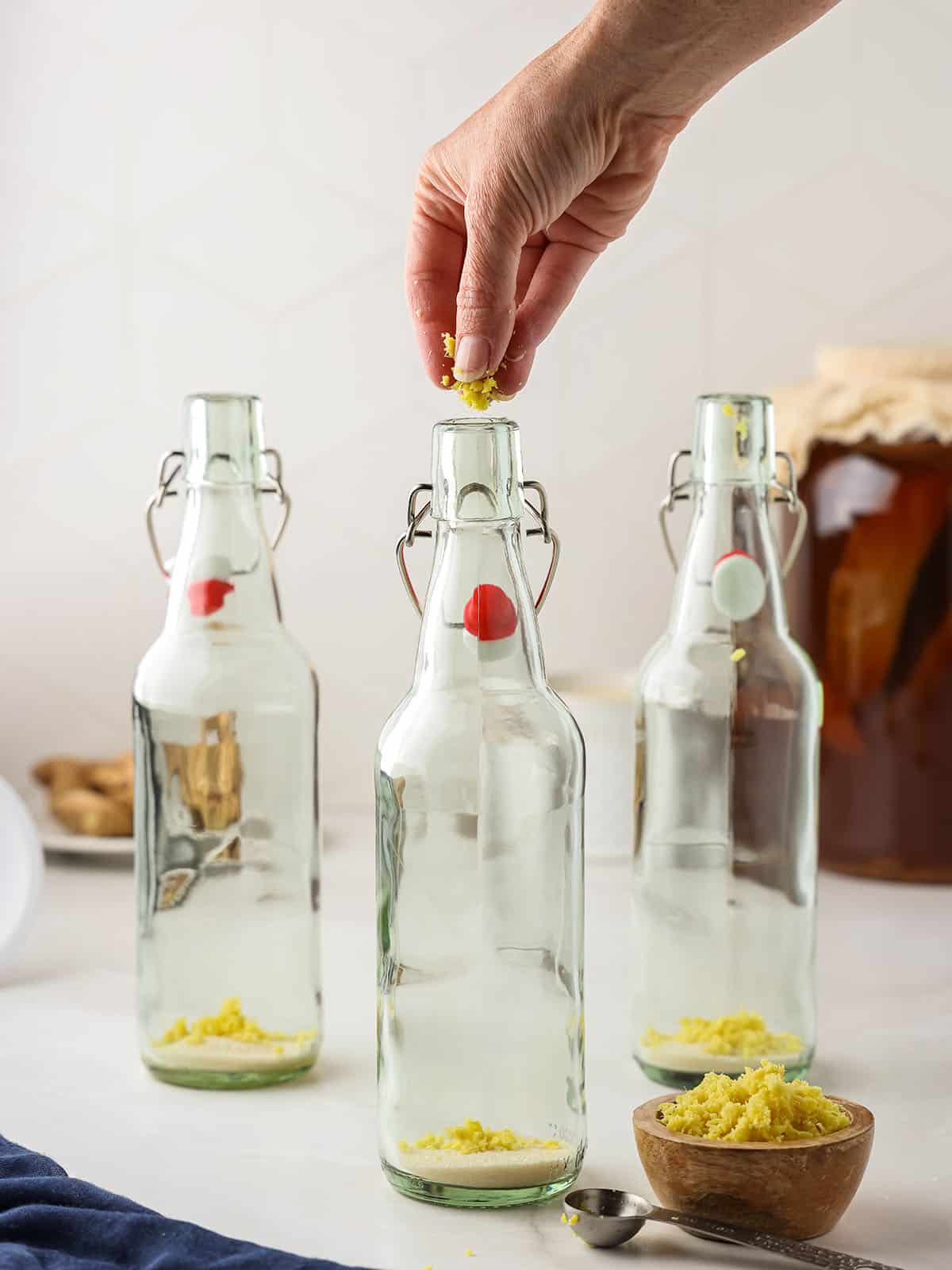 A hand putting minced ginger into flip top bottles. 