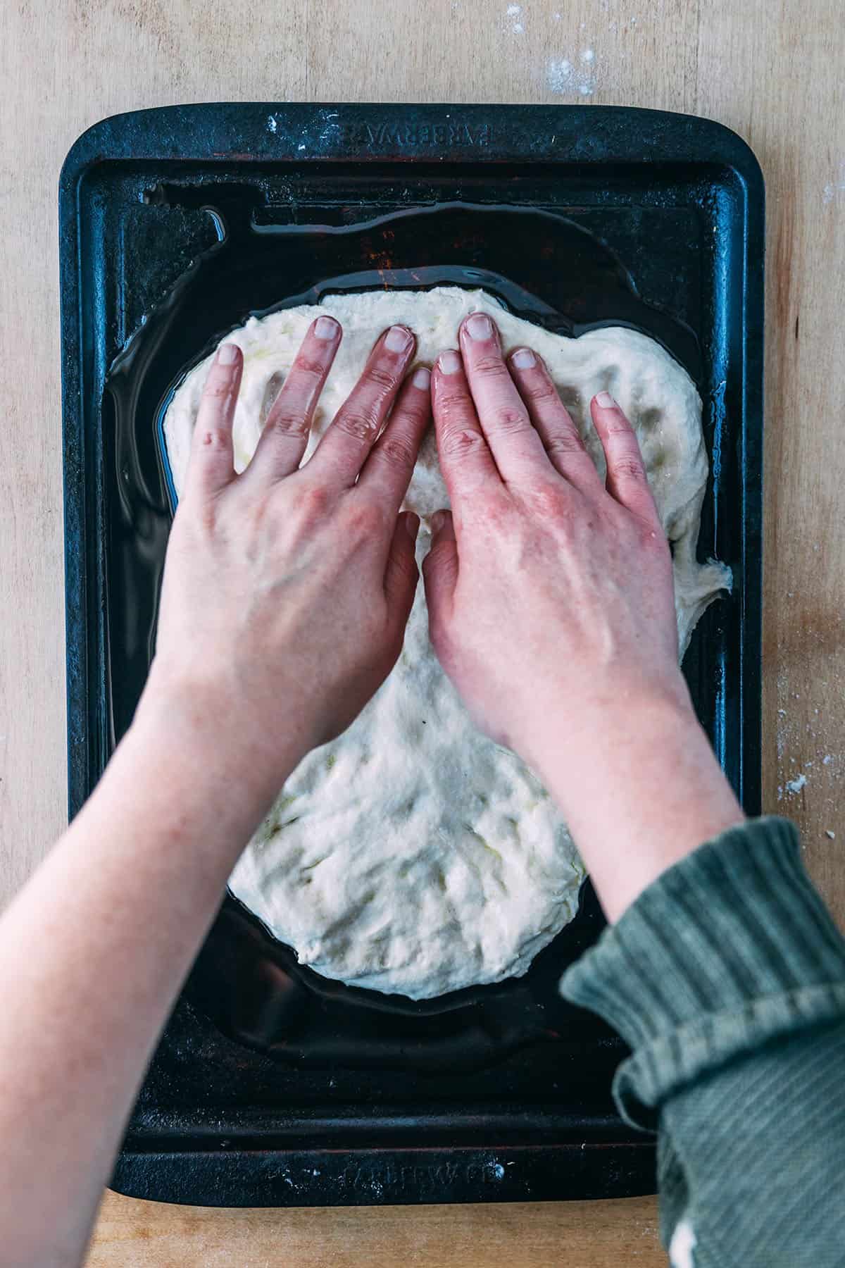 Sourdough pizza dough being shaped by two hands on a baking sheet. 
