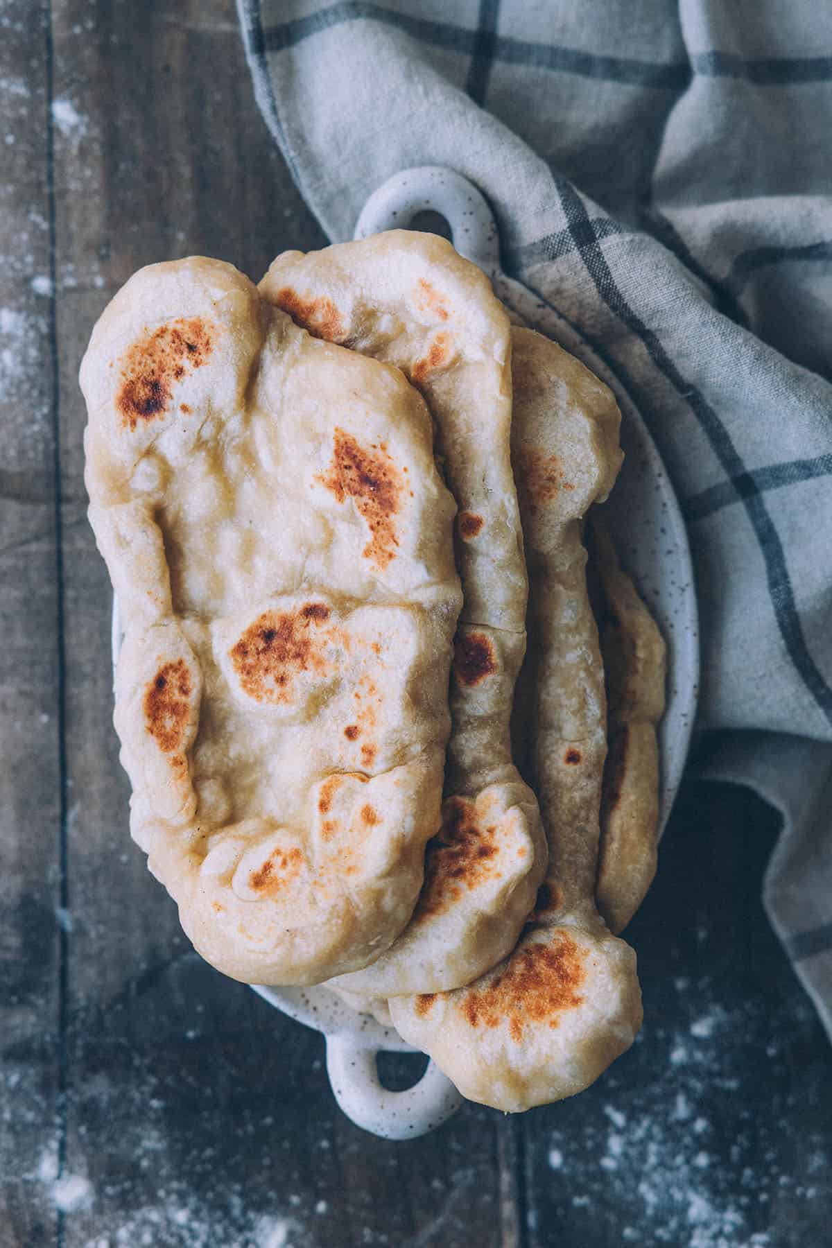 A stack of sourdough naan in a bowl on a wood surface, top view. 