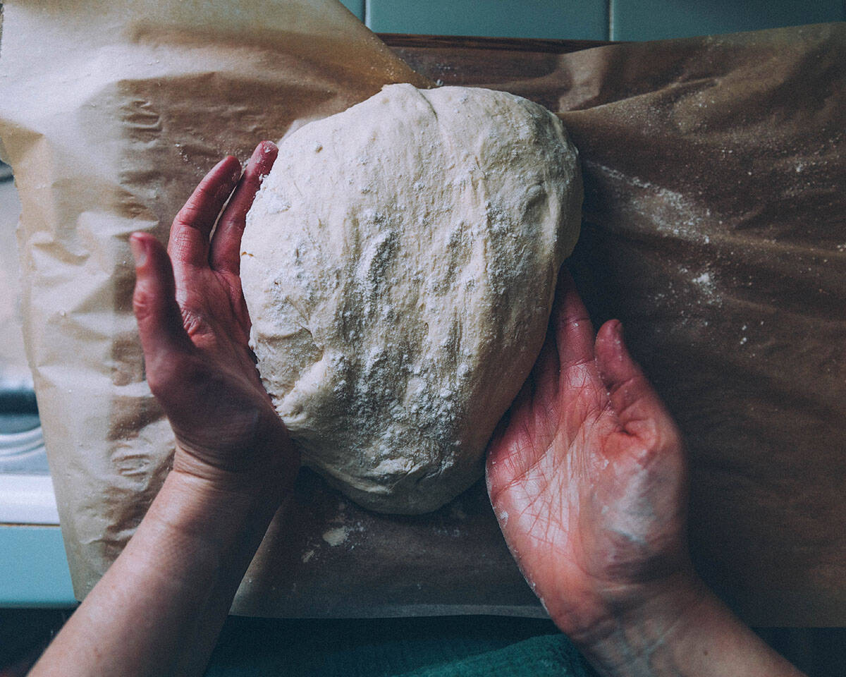 Hands kneading dough on a wood surface. 