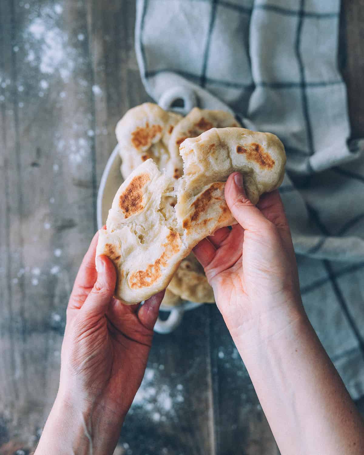 Naan bread in a stack lifted up and showing it breaking, top view above a wood surface. 