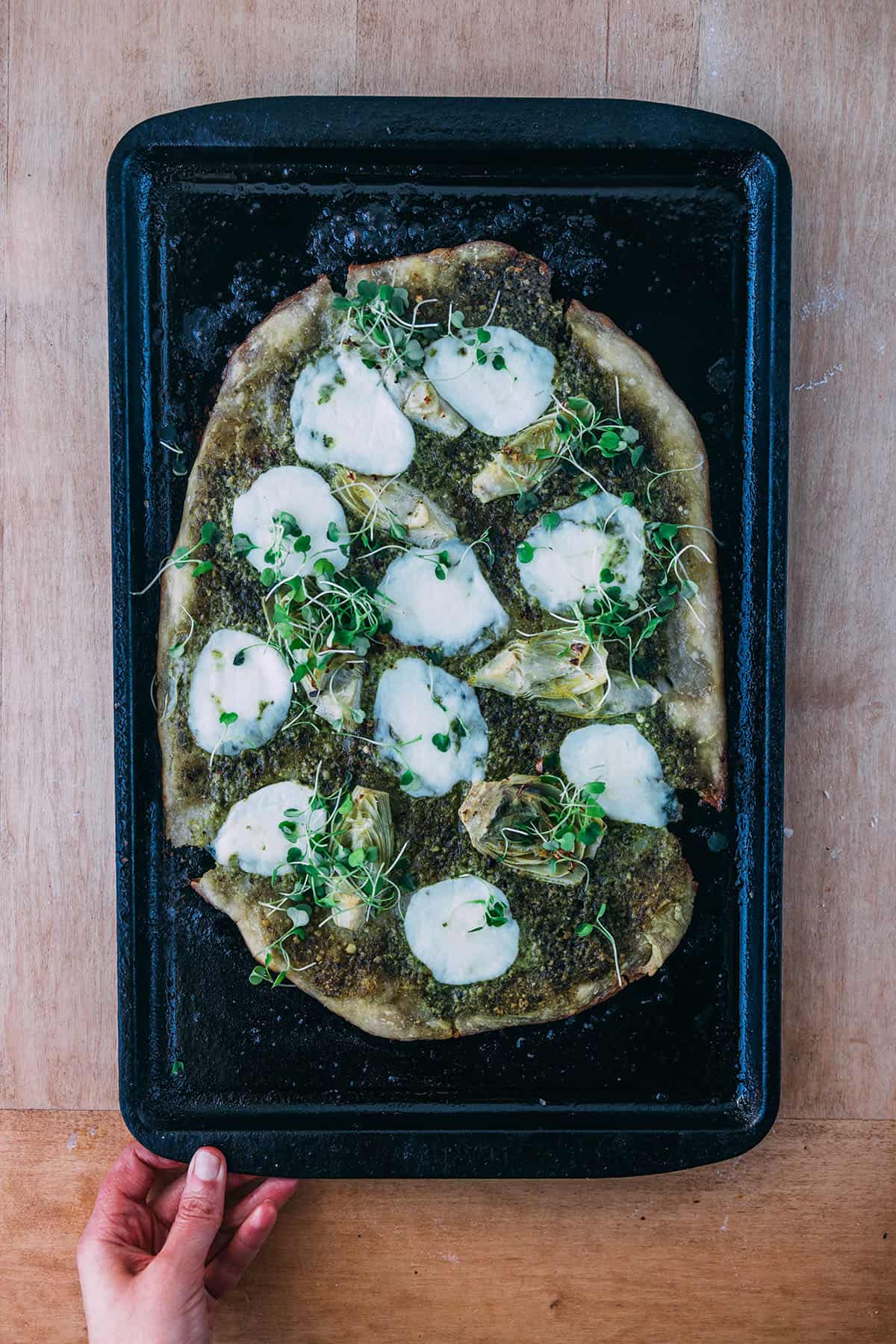 Baked sourdough pizza with pesto, mozzarella, and artichoke hearts. 