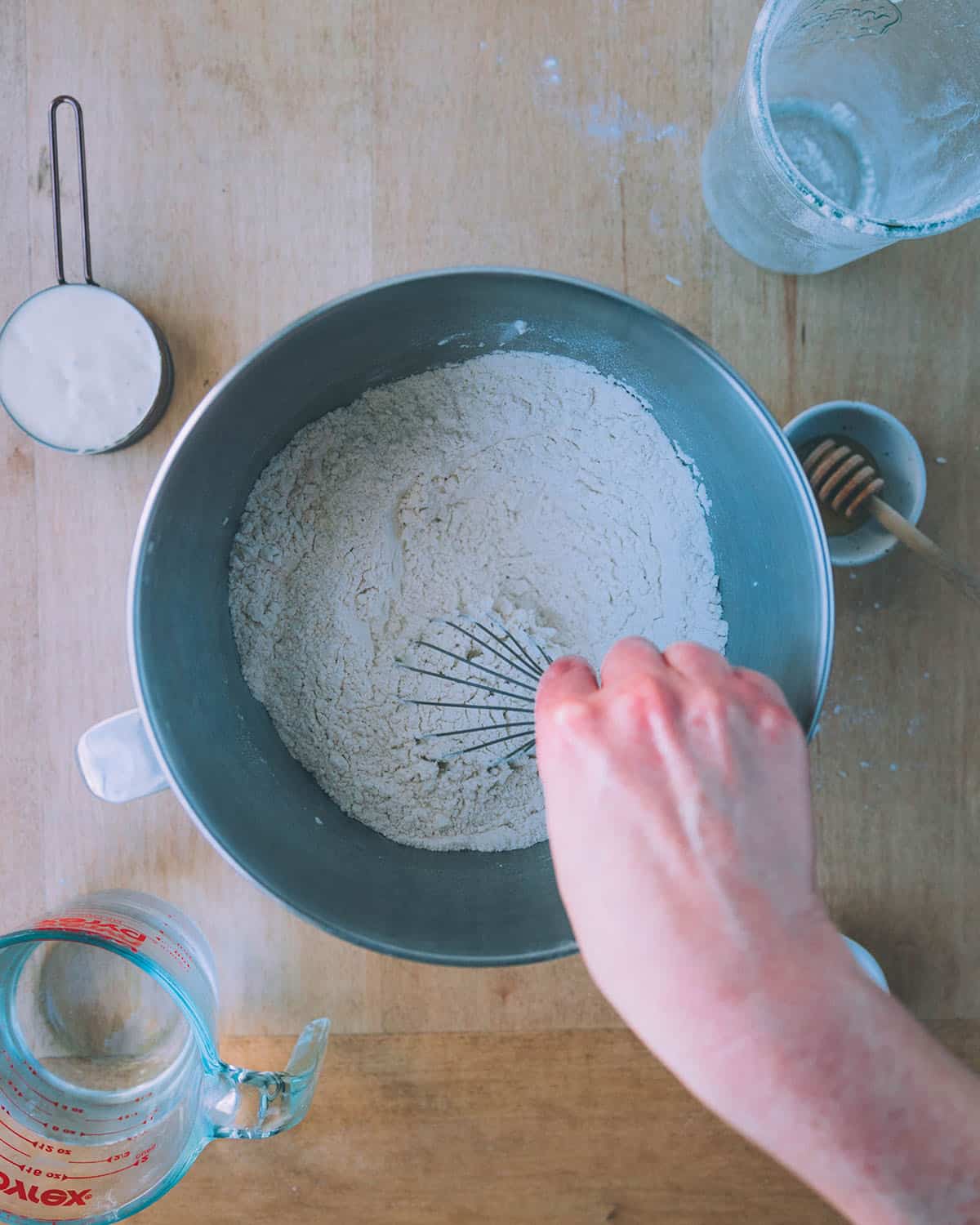 A hand whisking dry ingredients together to make pizza dough, top view. 