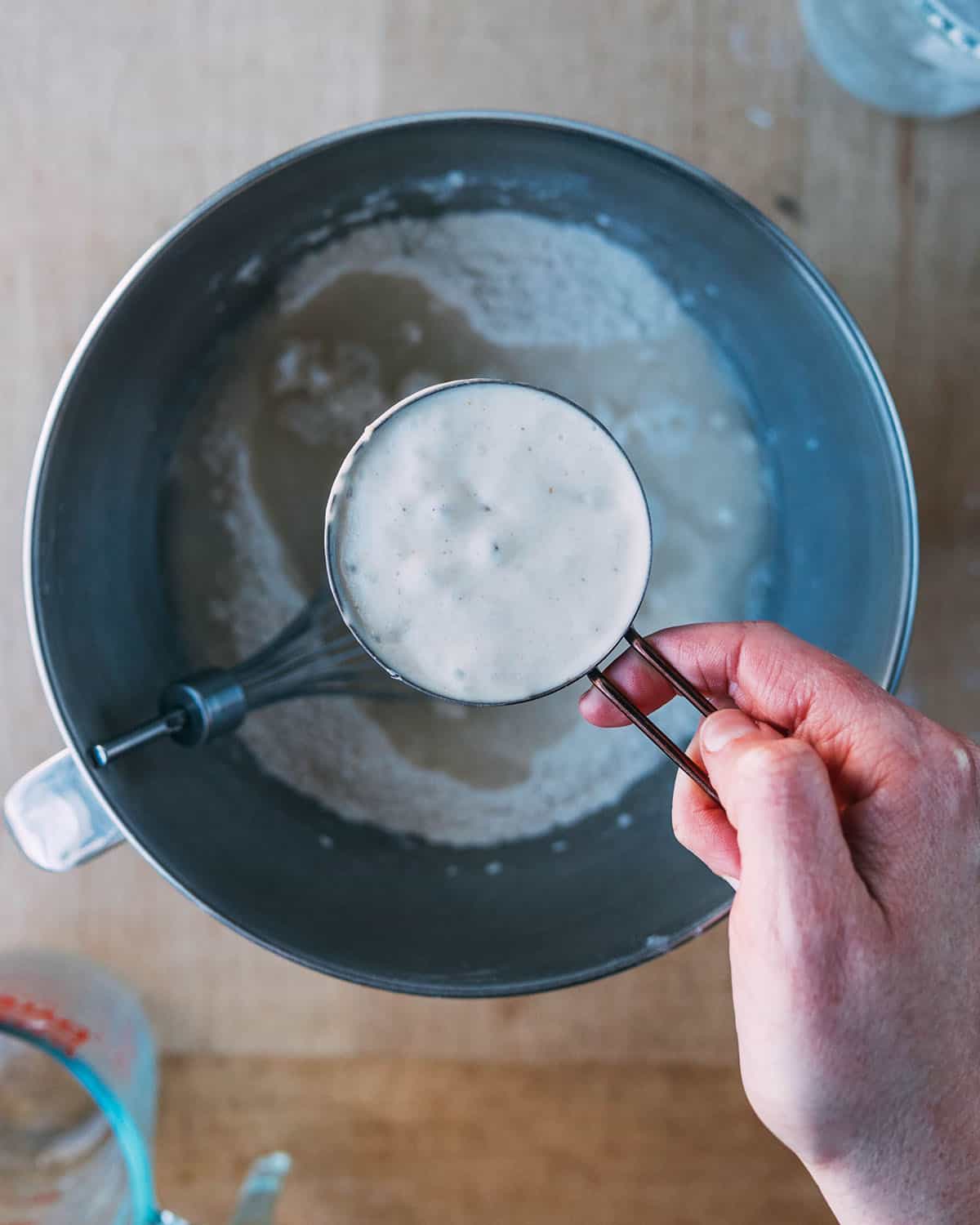 Sourdough starter pouring into the pizza dough bowl, top view. 