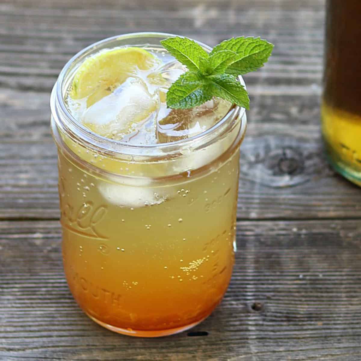 a mason jar glass of iced stinging nettle tea with a mint garnish on a wood table
