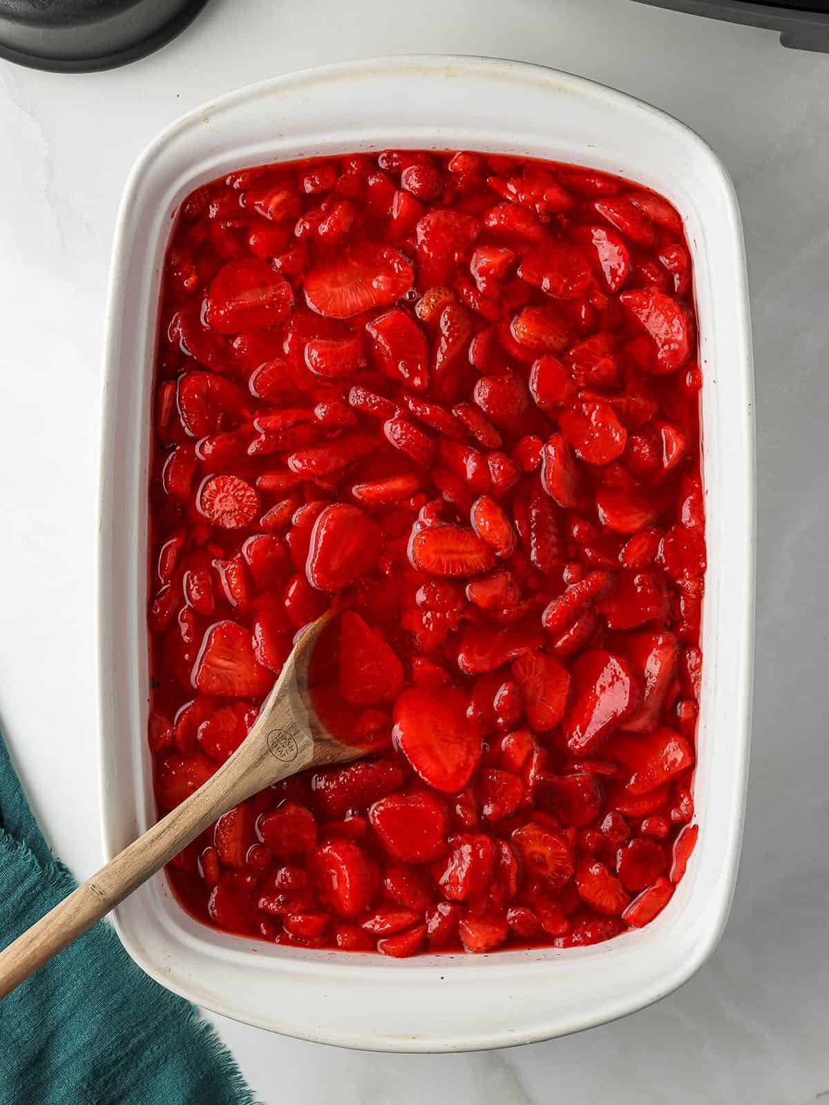 Strawberries sliced in a white baking dish with a wooden spoon in them.