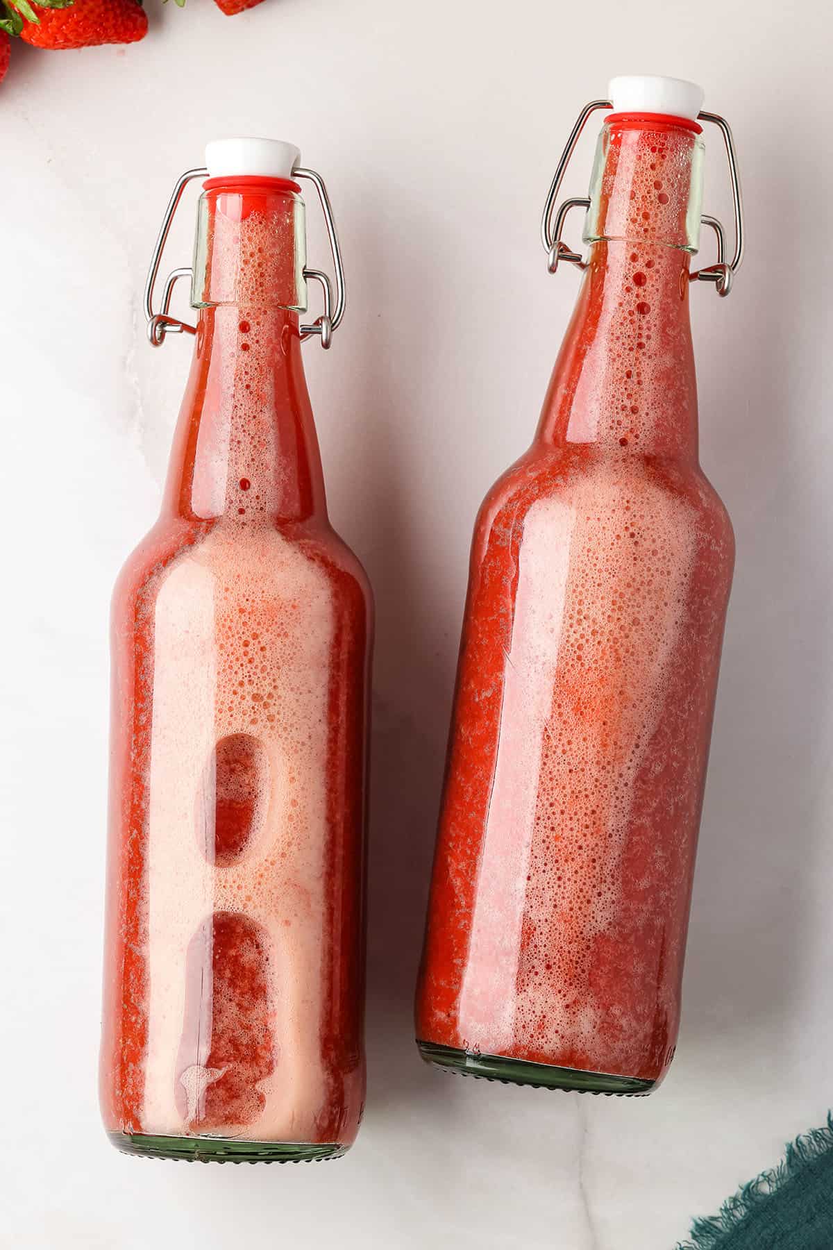 Closed flip top bottles with strawberry kombucha in them, laying on their sides on a white counter. 