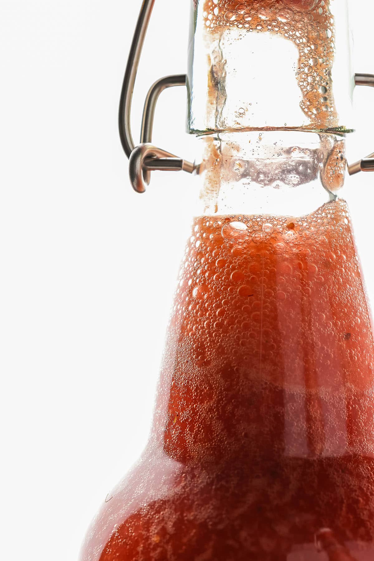 Close up of the top portion of a flip top bottle with strawberry kombucha in it, with about an inch of space at the top. 