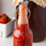 An open flip top bottle of red strawberry kombucha with lots of fizz at the top.