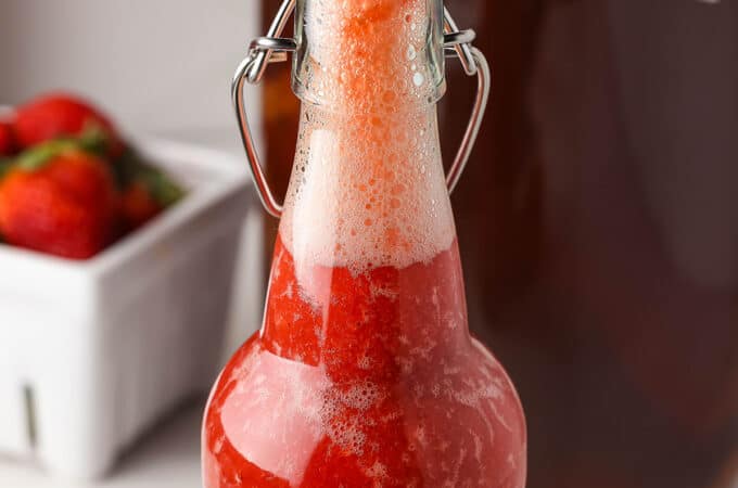 An open flip top bottle of red strawberry kombucha with lots of fizz at the top.
