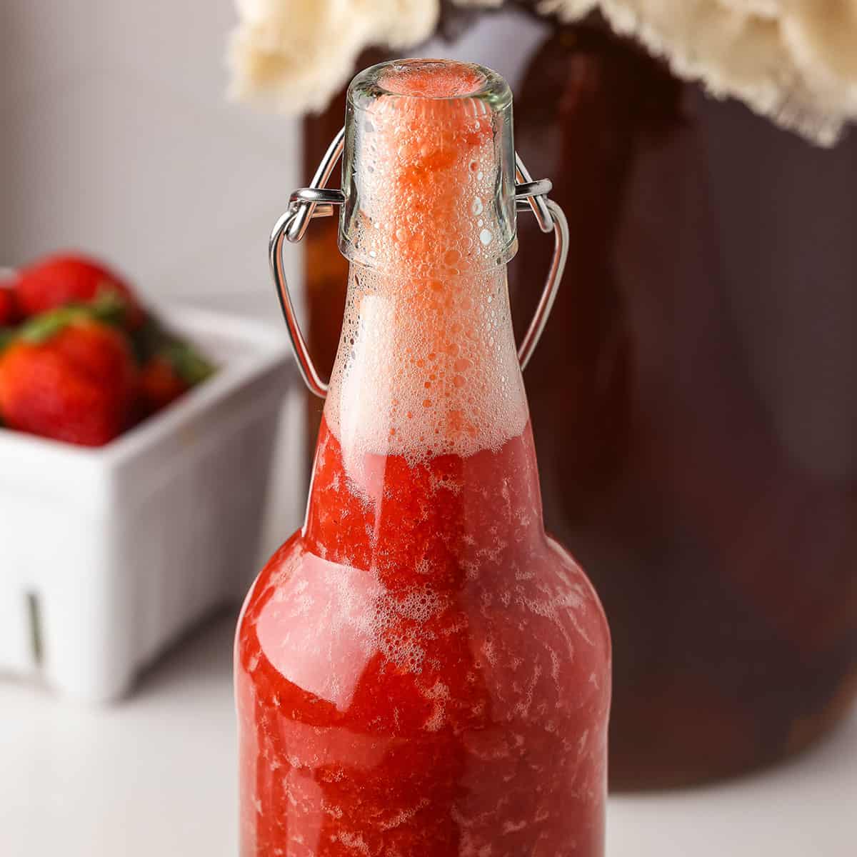 An open flip top bottle of red strawberry kombucha with lots of fizz at the top. 