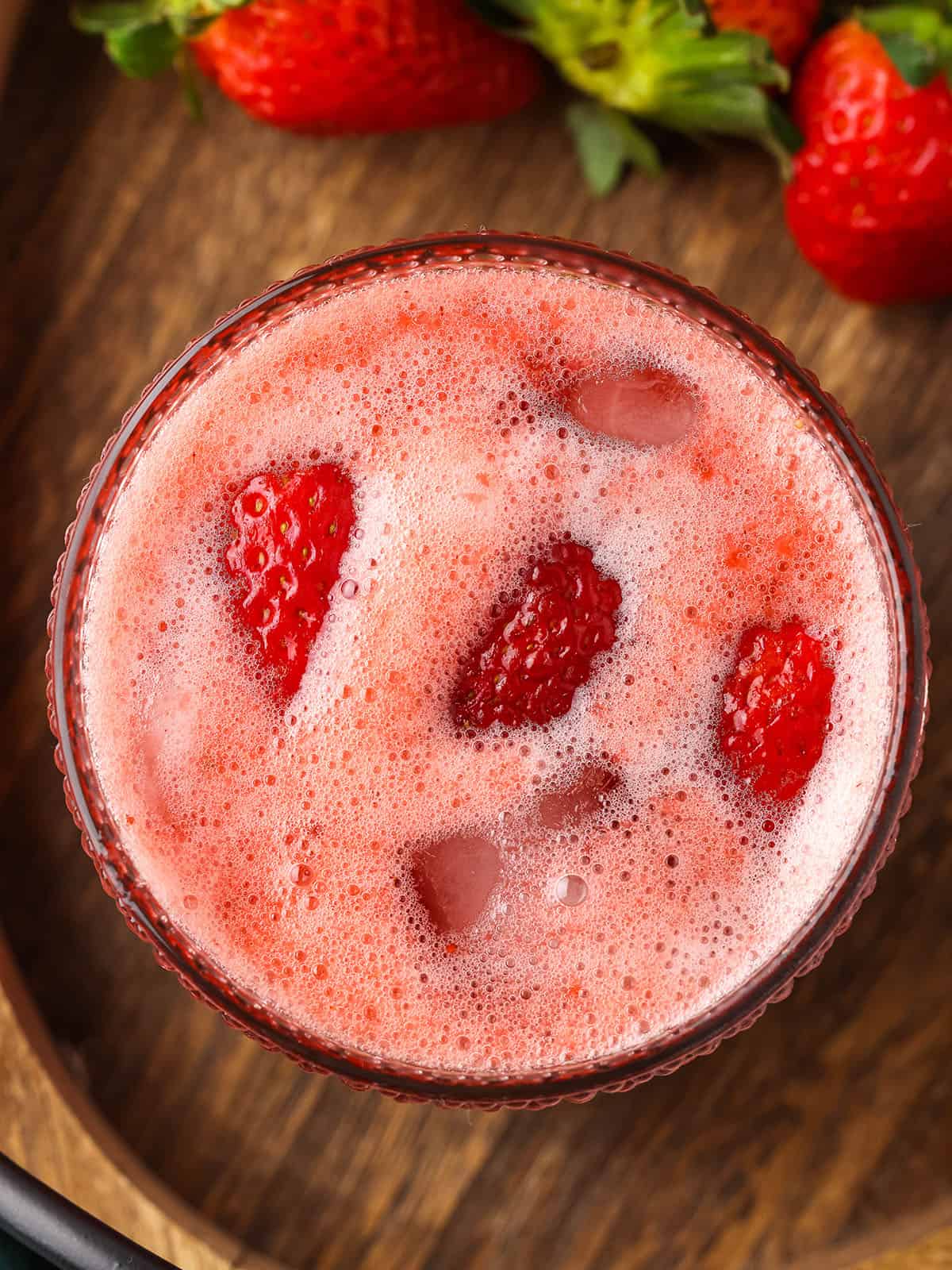 Strawberry kombucha with lots of pink fizz at the top in a cup with fresh strawberries floating in it, top view.