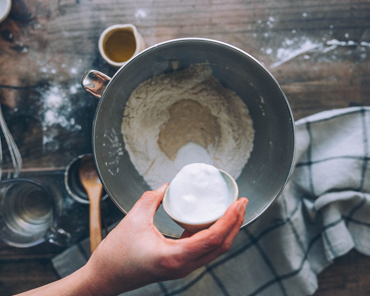 A hand pouring plain yogurt into a bowl with other naan bread ingredients. 