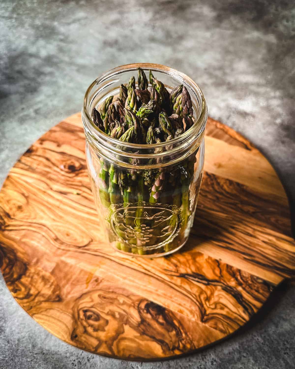 Asparagus in a jar with pickling spices on a wood cutting board. 