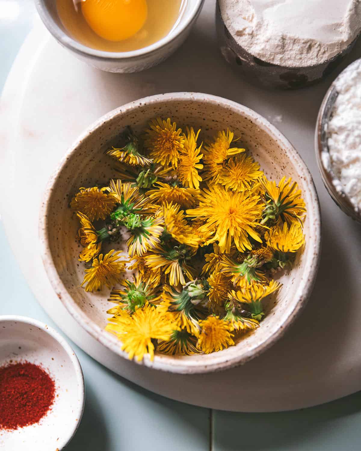 A white bowl of freshly foraged dandelion flowers, top view. 