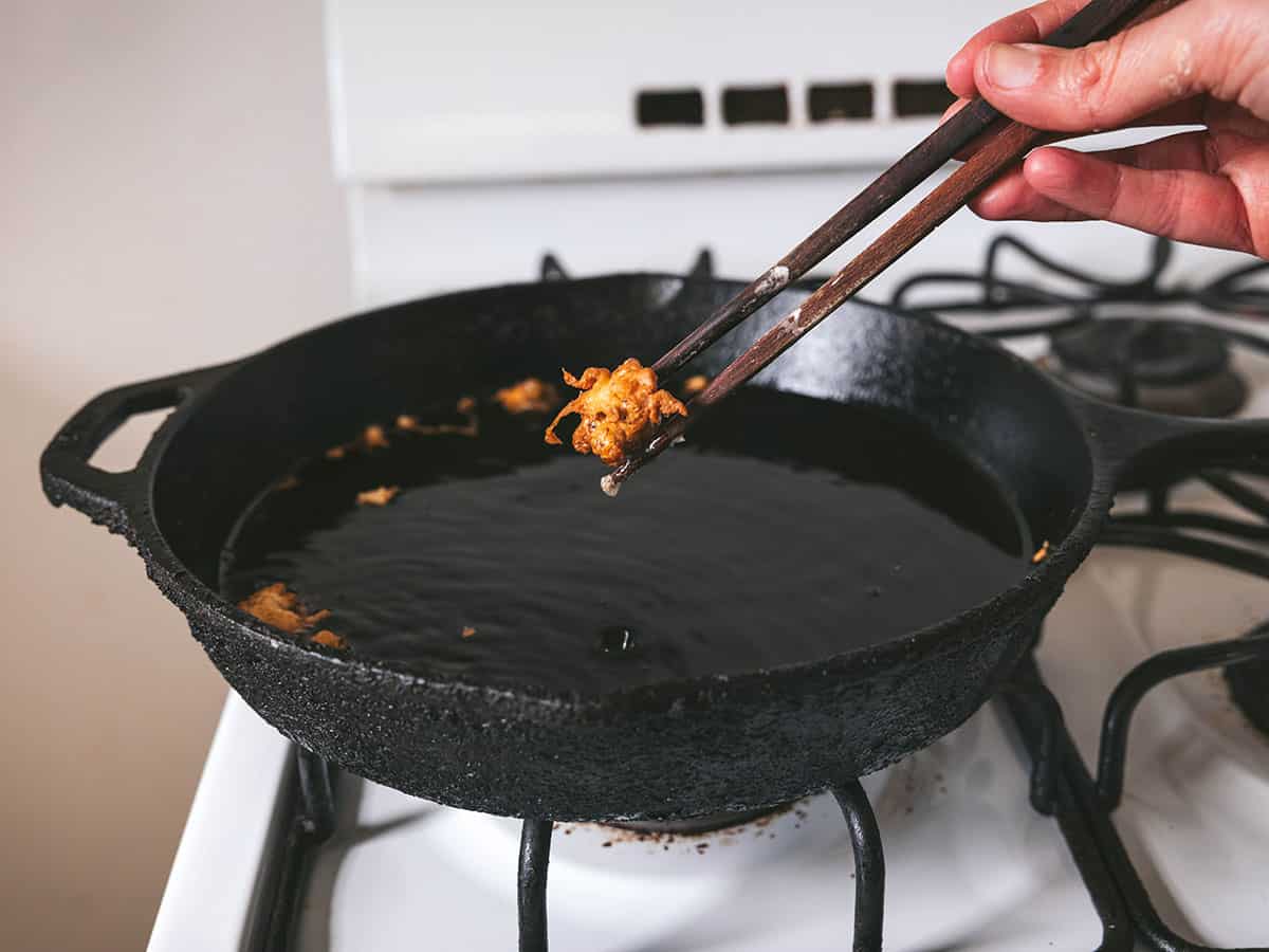 Chopsticks lifting golden brown dandelion fritters from a cast iron pan. 