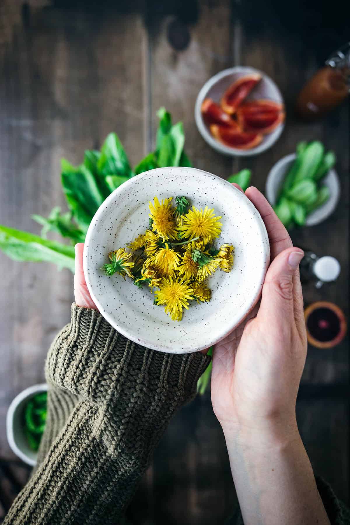 A hand holding up a small white bowl of dandelions for salad, top view. 