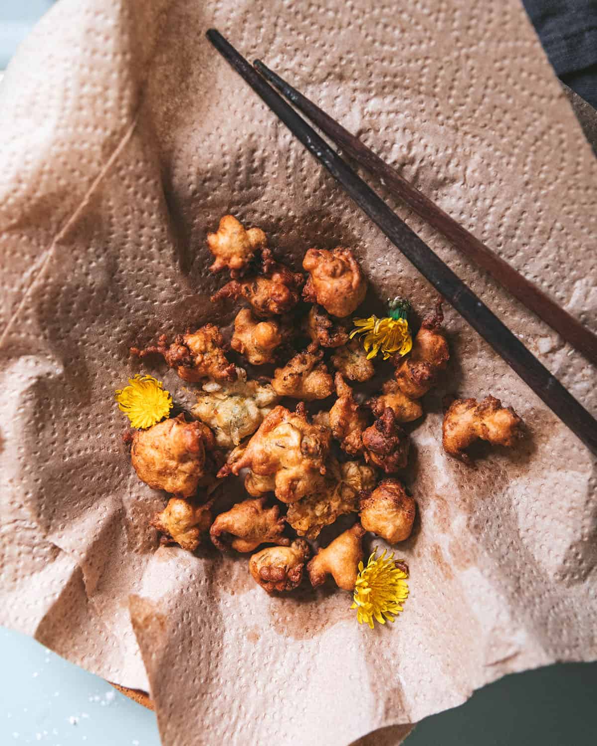Fried dandelion fritters on a natural napkin with chopsticks to the side, top view. 