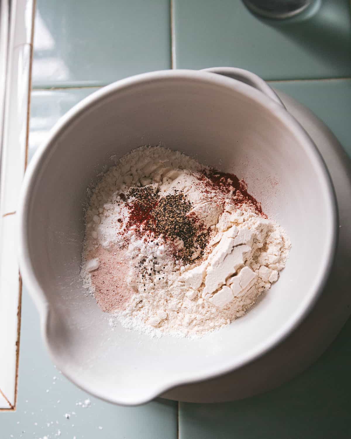 A white bowl with a wide pour spout with the dry ingredients for dandelion fritter batter in it, top view.