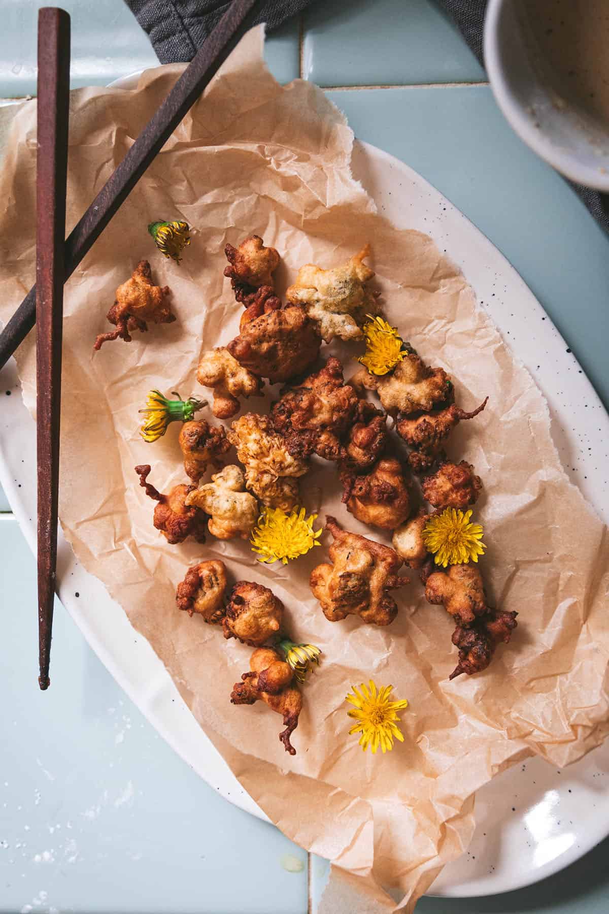 Dandelion fritters on an oval plate with a natural napkin and chopsticks, top view. 