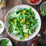 A fresh dandelion salad in a white bowl on a wood surface, top view.