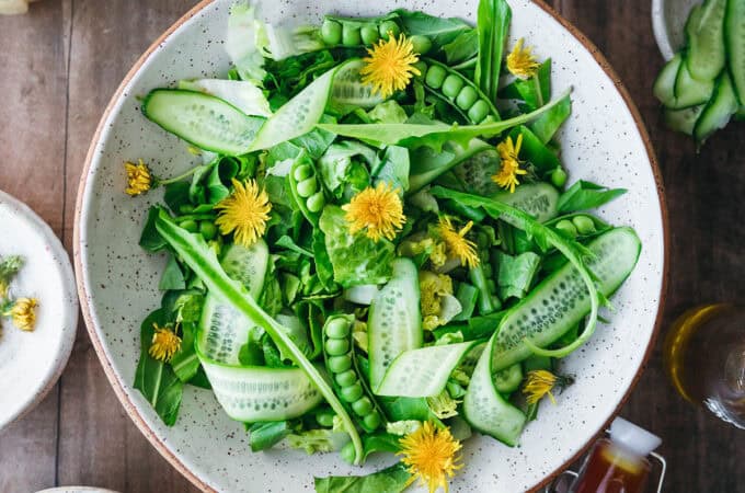 A fresh dandelion salad in a white bowl on a wood surface, top view.