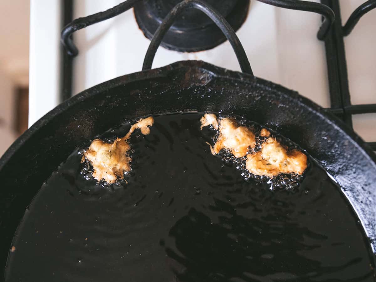 Dandelion fritters frying in a cast iron pan. 