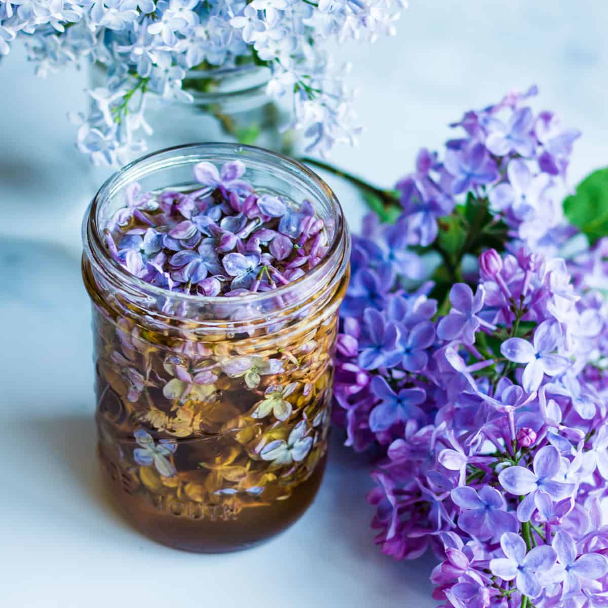 A jar filled with lilacs and honey, surrounded by fresh lilacs. 