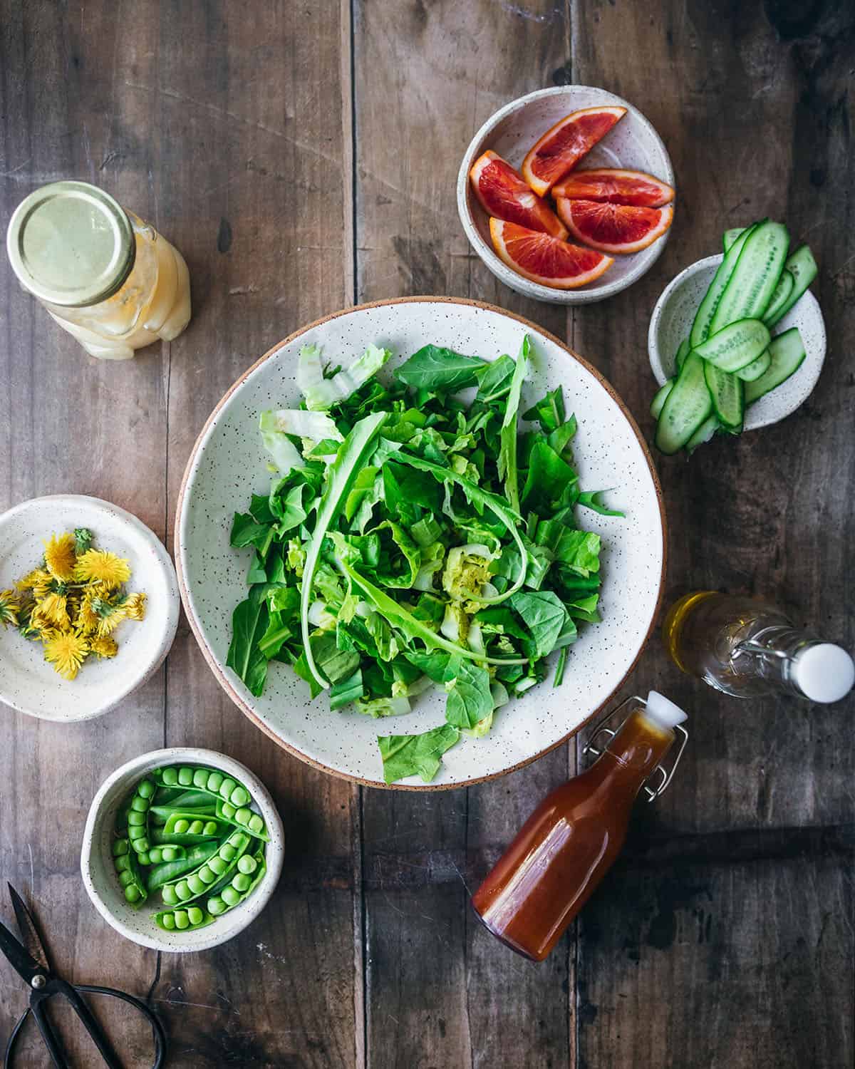 Dandelion greens chopped up in a white bowl, with other ingredients surrounding. Top view. 