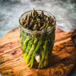 A jar of pickled asparagus on a wood surface.