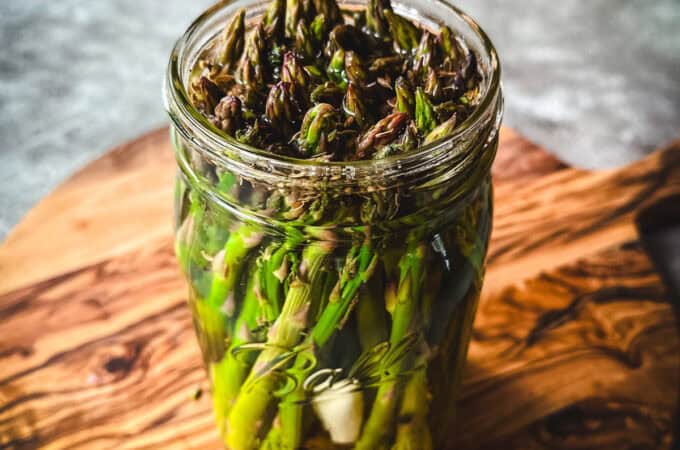 A jar of pickled asparagus on a wood surface.