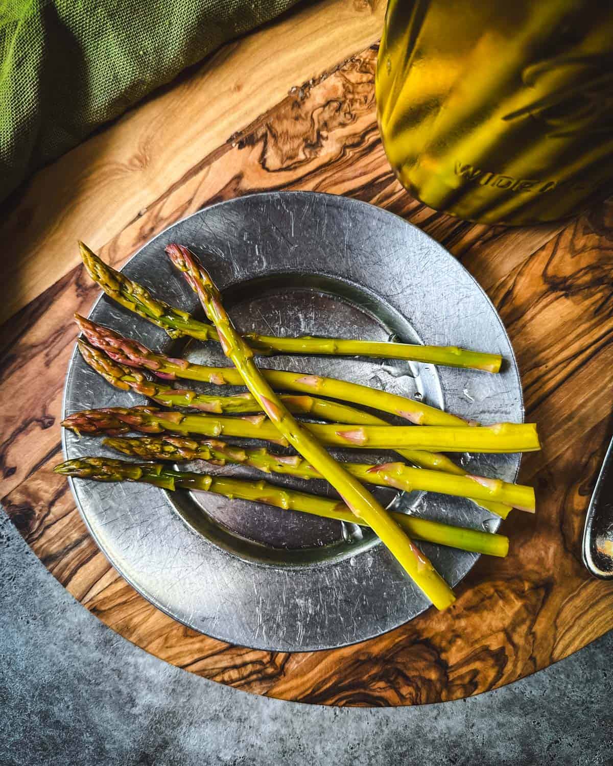 Pickled asparagus on a metal plate sitting on a wood cutting board, top view. 