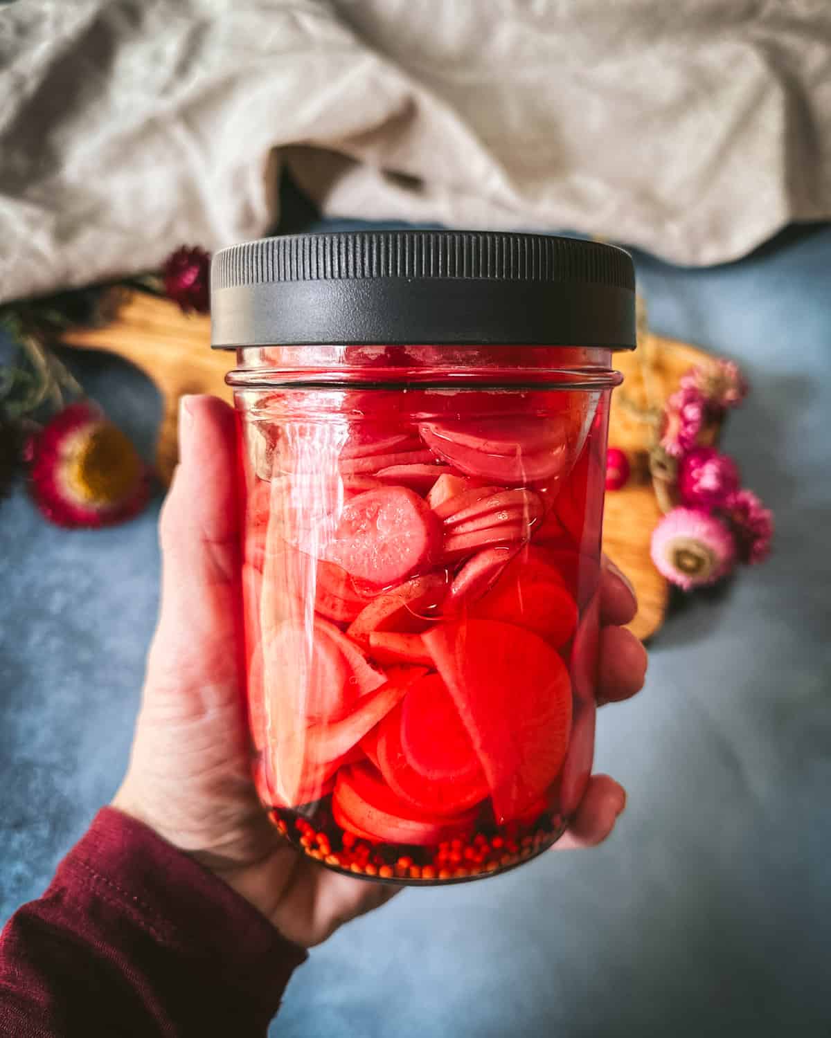 A hand holding up a jar of pink pickled radishes. 