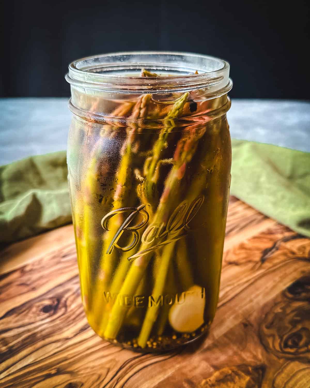 A jar of pickled asparagus on a wood cutting board. 