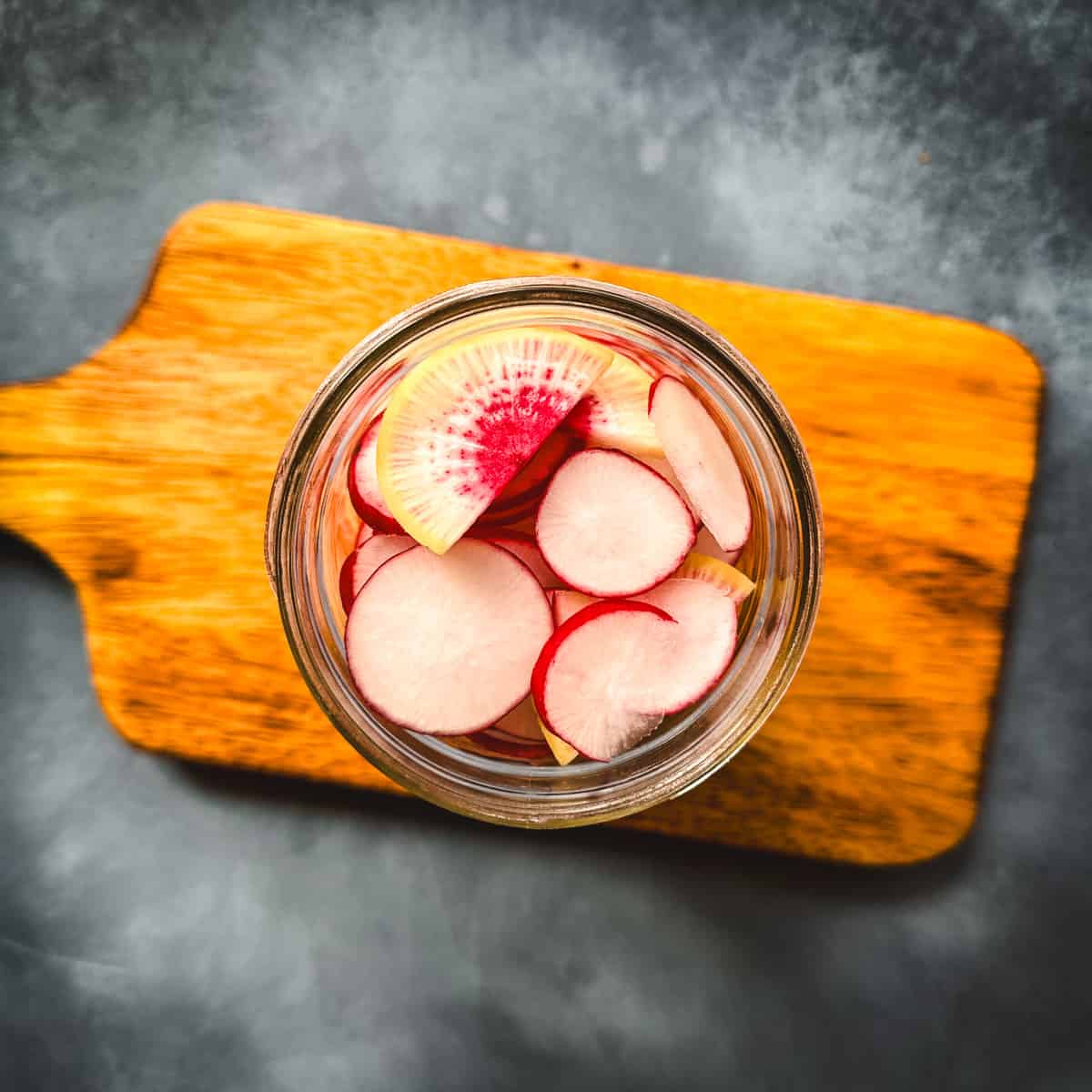 Sliced radishes in a jar, top view, on a wooden cutting board. 