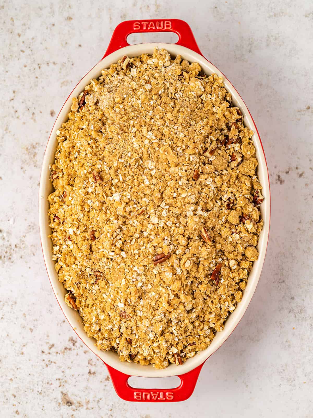 A red and white baking dish with rhubarb strawberry crisp ready to bake, top view. 