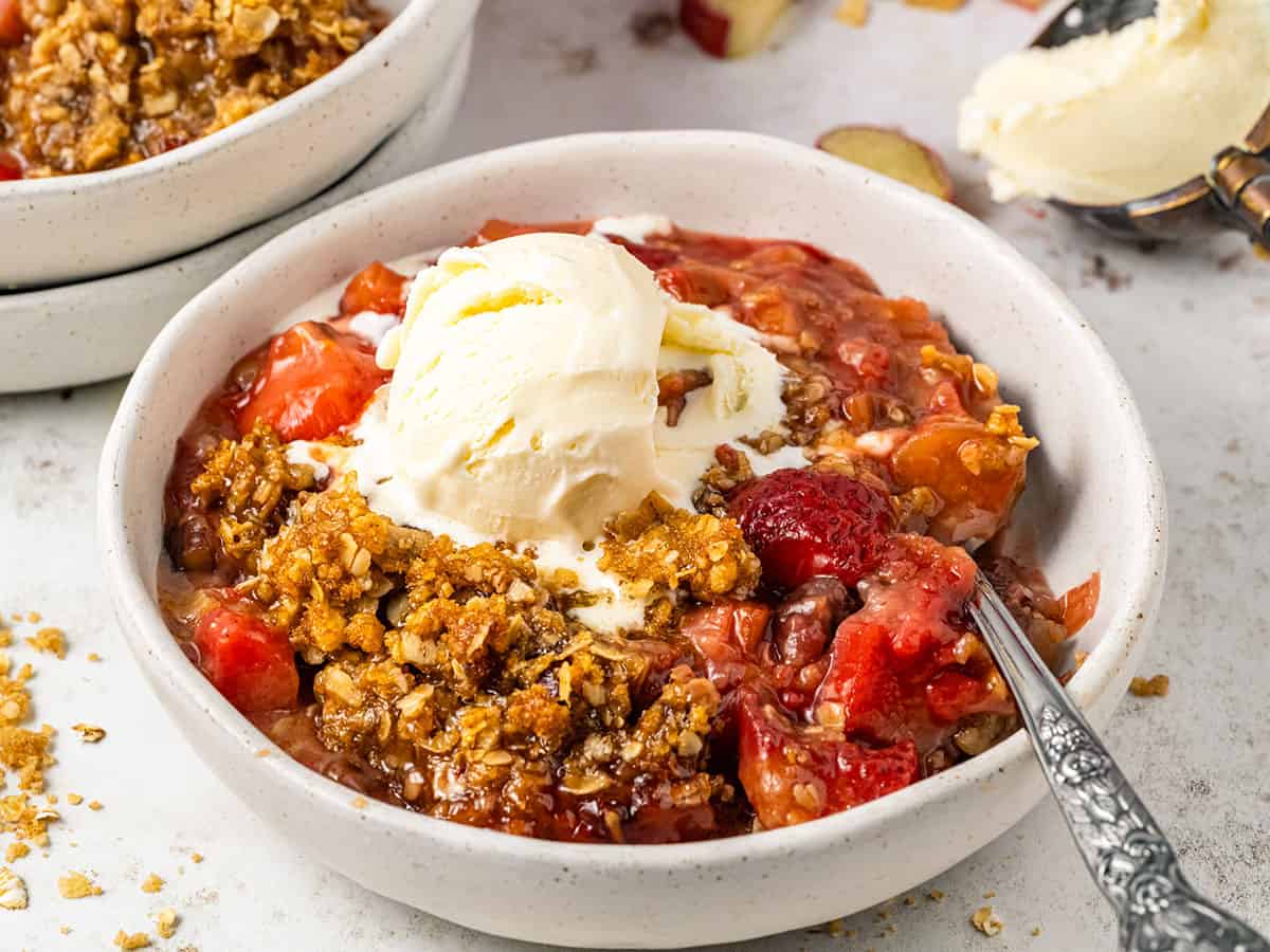 A bowl of rhubarb and strawberry crisp topped with ice cream. 