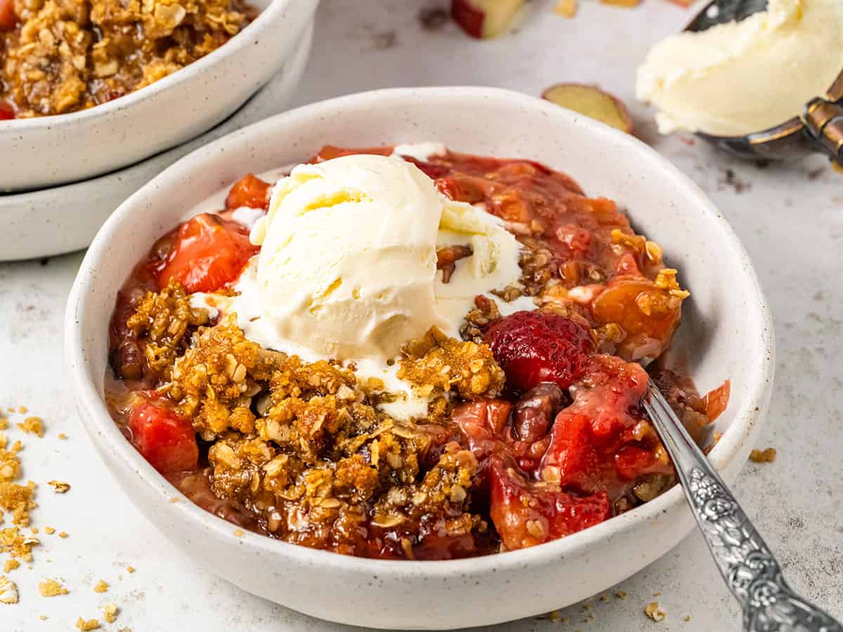 A bowl of rhubarb and strawberry crisp topped with ice cream.